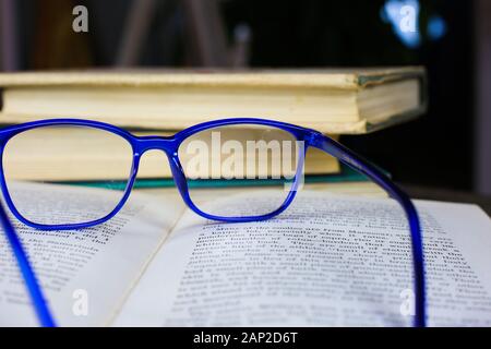 Blick auf alte open vergilbte Buch mit Blau Brille auf antiken Holztisch mit unscharfen Stapel Bücher Hintergrund Stockfoto