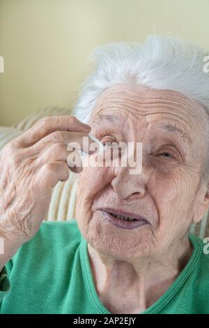 Eine ältere Frau Augentropfen, die in ihren Augen von sich zu Hause Stockfoto