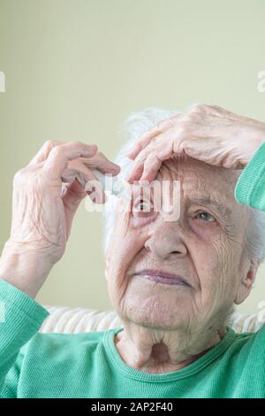 Eine ältere Frau Augentropfen, die in ihren Augen von sich zu Hause Stockfoto