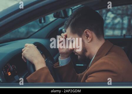 Ein junger Mann von 30 Jahren und hielt seinen Kopf, Kopfschmerzen, Auto fahren. Schlechte Gesundheit beim Fahren. Modische ungewöhnliche Schatten in warmen Farben. B Stockfoto