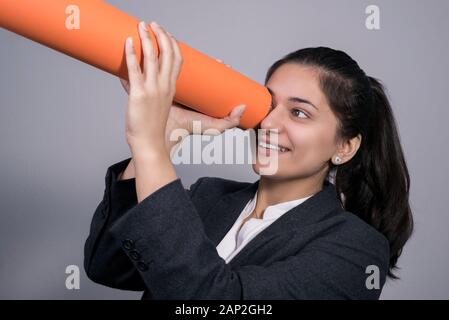 Porträt einer schönen Indischen jungen Geschäftsfrau in einem Anzug, Holding a Twisted orange Rohr in der Hand, in die Sie suchen. Freier Platz. Studio Stockfoto