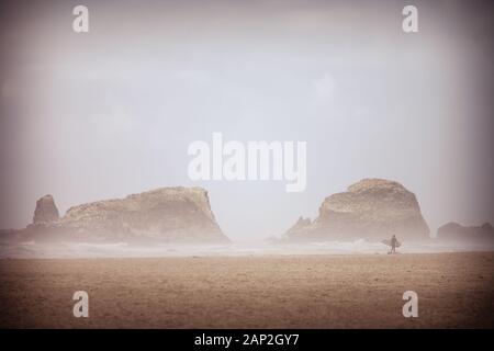 Surfer wandern entlang einer Küstenlinie von Sand und Felsen auf Ecola State Park Strand von Oregon USA Stockfoto