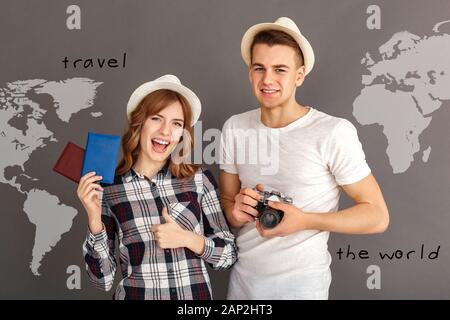 Reise und Tourismus. Junger Mann mit Kamera und Frau mit Pässen, Daumen hoch für Hüte isoliert auf Grau lächelnd verspielten stehend Stockfoto