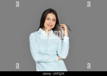 Freistil. Junge Frau steht isoliert auf grauem Spiel mit haarfreudigen Haaren Stockfoto