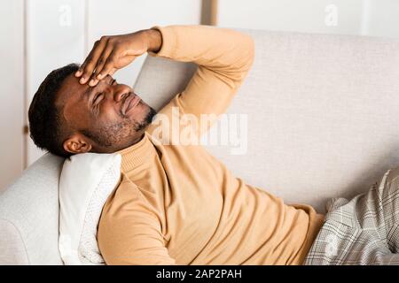 Mann, der Kopfschmerzen leiden unter Schmerzen auf der Couch liegend Indoor Stockfoto