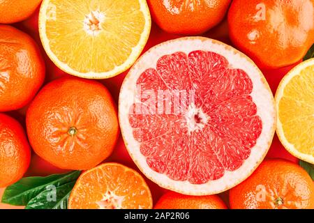 Frische reife Mandarinen, Grapefruits und Orangen mit grünen Blättern auf orangem Hintergrund. Nahaufnahme, Ansicht von oben. Stockfoto