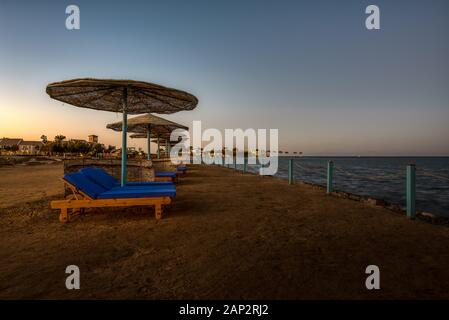 Liegestühle und Sonnenschirme am Abend bei Sonnenuntergang entlang der Küstenlinie in El Gouna, Ägypten, 6. Januar 2020 Stockfoto