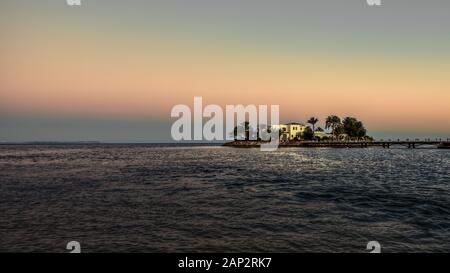 Weiße Villa auf einer kleinen Insel mit Palmen und eine Brücke, die in der Dämmerung Abend licht, El Guna, Ägypten, Januar 07, 2020 Stockfoto