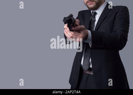 Portrait eines bärtigen Mann in einem Anzug hält eine Ziel Revolver. Auf grauem Hintergrund. Kriminelle Typ Mann, Gangster, Killer, Geschäftsmann killer Stockfoto