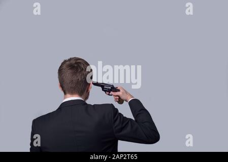 Portrait eines bärtigen Mann in einen Anzug, mit dem Rücken, mit einem Revolver in der Hand, sich selbst anstrebt. Auf grauem Hintergrund. Crimina Stockfoto