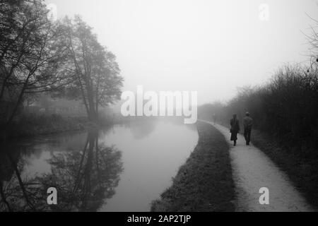 Am frühen nebligen Morgen am Trent and Mersey Kanal (Staffordshire, Großbritannien). Paar geht auf den Fußweg, der in die Ewigkeit geht Stockfoto