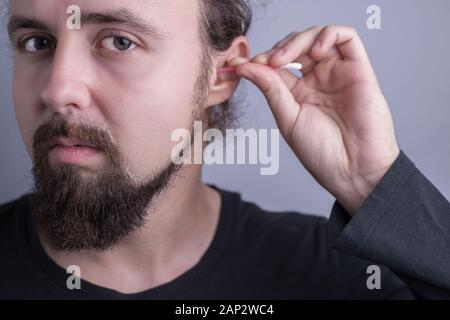 Portrait einer jungen bärtigen Kerl. Nahaufnahme von einem Mann mit einem Wattestäbchen zu reinigen Schwefel in seinen Ohren. Ohr, Gesundheit, Pflege und Reinigung. Die Perforation des Stockfoto