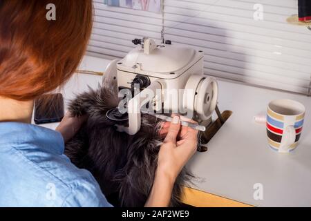 Professioneller Meister in der Herstellung von Bekleidung aus Pelz. Frau Couturier an der Nähmaschine. Der Prozess des Nähens von Fellkleidung. Designer Pelz Co Stockfoto