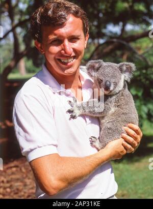 Junger Mann, der Koala (Phascolarctos cinereus) im Lone Pine Koala Sanctuary, Feigenbaumtasche, Brisbane, Queensland, Australien hält Stockfoto