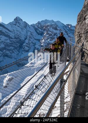 Menschen, die auf dem Thrillerspaziergang bei Birg in den Alpen, Schweiz, spazieren gehen. Es handelt sich um einen Stahlweg, der in die Cliffside integriert ist und darunter einen senkrechten Tropfen hat. Stockfoto