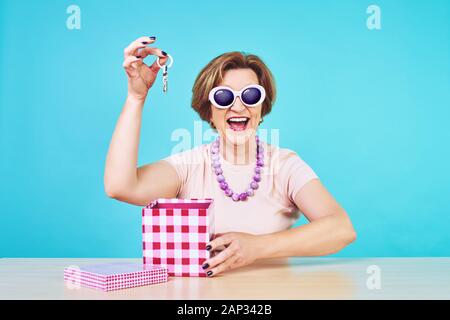 Lustige aufgeregt, alte Frau. Eine alte Frau war sehr happy house Tasten als Geschenk zu empfangen. Geöffnet vorhanden, über blau Hintergrund isoliert. Stockfoto