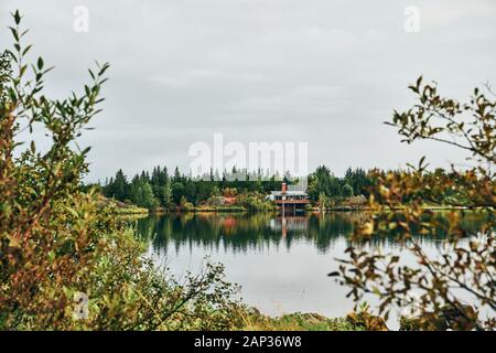 Durch Laub Ansicht des Hauses am gegenüberliegenden Ufer des Flusses unter bunten Pflanzen und Bäume auf Wetter Stockfoto