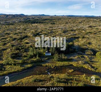 Von oben malerische Landschaft von einsamen Hütte auf Glade unter grünen Bäumen, in der Nähe von Bach mit transparenten Wasser gegen nebligen Hochland bei Horizon u Stockfoto