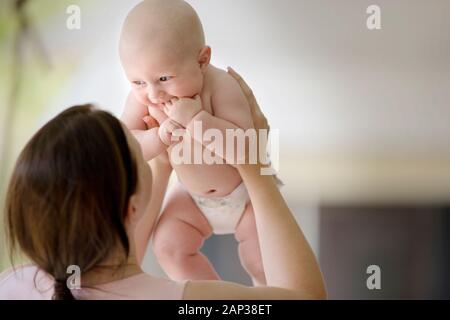 Smiling baby aloft von seiner Mutter gehalten wird. Stockfoto