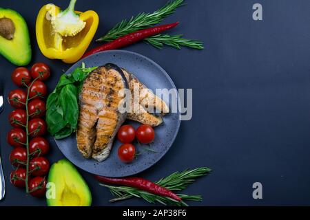Zwei frischen, rohen Lachs Steaks mit Gemüse und Gewürze: Rosmarin, Tomaten, Paprika, Basilikum, Zitrone und Olivenöl auf einem grauen Platte auf schwarzen Hintergrund. T Stockfoto