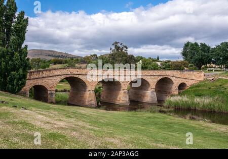 Richmond, Tasmanien, Australien - 13 Dezember, 2009: Landschaft und gesamte braun Stein historische Brücke über Coal River unter Blau cloudscape mit grünen l Stockfoto