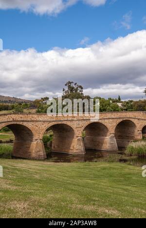 Richmond, Tasmanien, Australien - 13 Dezember, 2009: Abstand Portrait von braunem Stein historische Brücke über Coal River. Grünes Laub am Ufer und im Wat Stockfoto