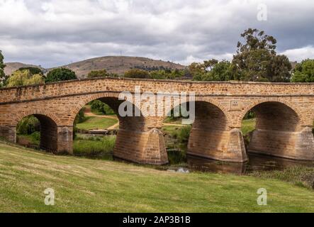 Richmond, Tasmanien, Australien - 13 Dezember, 2009: Landschaft geschossen von braunem Stein historische Brücke über Coal River unter dunklen cloudscape. Grünes Laub Stockfoto