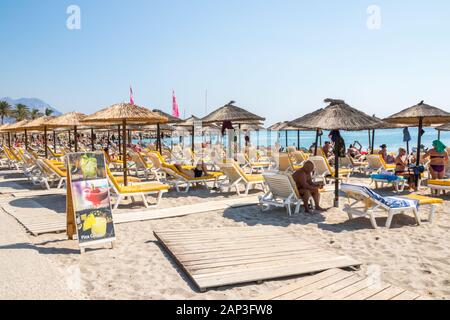 Kardamena an, Kos, Griechenland - 20. September 2019: Menschen auf Liegestühlen unter Sonnenschirmen am Strand der Stadt ist ein beliebtes Urlaubsziel. Stockfoto