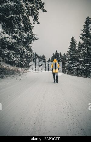 Junger Mann, der in der Winterlandschaft auf dem Waldweg in gelber Jacke spazieren geht Stockfoto