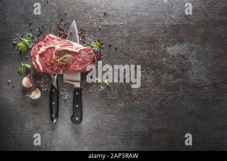 Rohes Rindfleisch Steak mit Messer und Gabel Salz Pfeffer und Kräutern auf dunklen konkreten Hintergrund Stockfoto