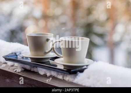 Dampfend heißer Kaffee in zwei Tassen, im Schnee begraben, auf einem Balkon, an einem strahlenden Wintermorgen. Frühstück für zwei. Gemütliche winter Konzept. Stockfoto