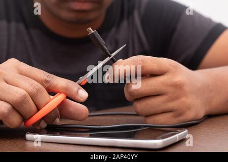 Hände, die das Micro-USB-Lade- und Datenkabel oder -Kabel mit Schere schneiden. Stockfoto