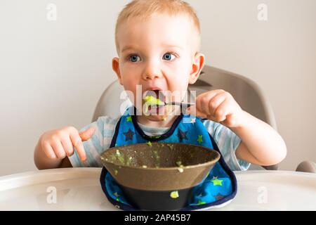 Kleiner Junge allein isst Püree aus einer Platte. Stockfoto