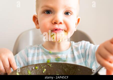 Kleiner Junge allein isst Püree aus einer Platte. Stockfoto