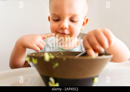 Kleiner Junge allein isst Püree aus einer Platte. Stockfoto