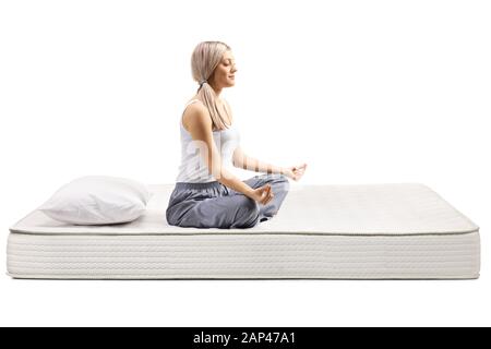 Junge Frau in den Schlafanzügen Sitzen auf einer Matratze in einer Meditation Pose auf weißem Hintergrund Stockfoto