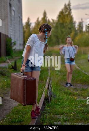 Ein junges Mädchen mit einem Koffer steht auf den Schienen zurück zu ihrer Freundin im Hintergrund. Stockfoto