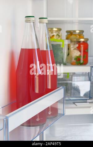 Glasflaschen mit hausgemachtem roten Beerensaft und Gläsern mit eingelegtem Gemüse stehen im Kühlschrank. Fermentiertes, gesundes Naturlebensmittelkonzept. Stockfoto