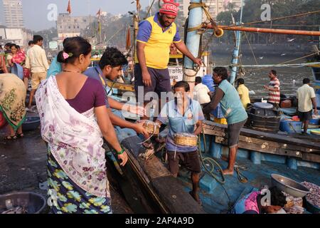 Fischer an den Sassoon Docks, einem Fischerhafen in Colaba, Mumbai, Indien, die am Pier Körbe mit ihrem Fang an Händler weitergeben Stockfoto