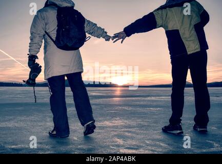 Paar hat Spaß im Winter zu Fuß auf dem Eis der gefrorenen See. Abend Wanderung am Strand von Teich. Warme Kleidung Paar mit hohen warme Stiefel. Stockfoto