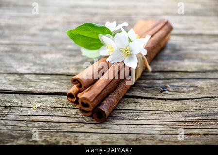 Zimtstangen und Jasminblüte auf Vintage-Holztisch. Nahaufnahme von Kräutern und Gewürzen. Natürliches würziges Aroma. Aromatherapie Zen Stillleben. Stockfoto