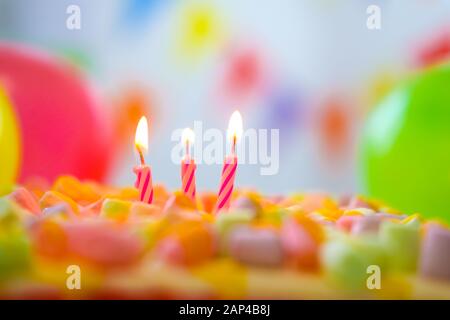 Festliche bunte Geburtstagskarte mit drei brennenden Kerzen auf Regenbogenkuchen und bunten Luftballons im Hintergrund. Platz für Glückwunschtexte Stockfoto