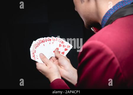 Zauberer zeigt Trick, indem er dieselben Karten auf dunklem Hintergrund spielt. Offenlegung des Fokus Stockfoto