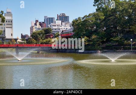 Blick auf den Kawazokoike Teich mit Springbrunnen und die rote Brücke im Tennoji Park von Osaka. Japan Stockfoto