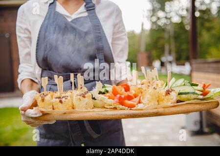 Catering-Service. Der Kellner in der Schürze trägt Imbisse auf der Platte Stockfoto