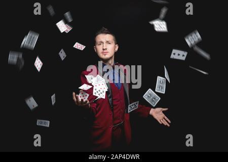 Der illusionistische Zauberer zeigt Magie mit Spielkarten auf schwarzem Hintergrund Stockfoto