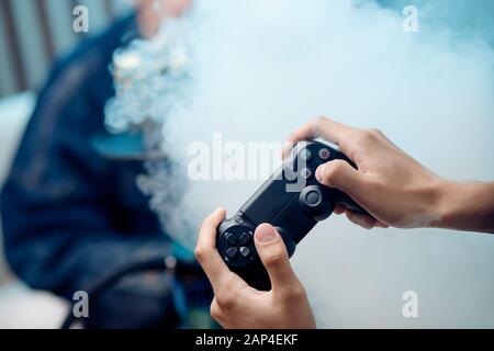 Mann hält Gamepad in den Händen, im Hintergrund Rauch von Hookah Stockfoto