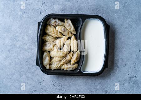 Nehmen Sie den georgischen Knödel Khinkali mit Fleisch, Tomaten, Gewürze und Joghurt in Kunststoff Box Container Paket/Hingel. Bereit zu Essen. Stockfoto