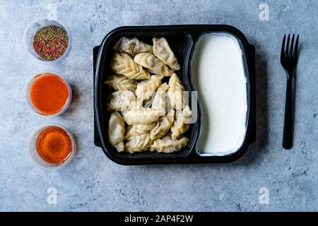 Nehmen Sie den georgischen Knödel Khinkali mit Fleisch, Tomaten, Gewürze und Joghurt in Kunststoff Box Container Paket/Hingel. Bereit zu Essen. Stockfoto