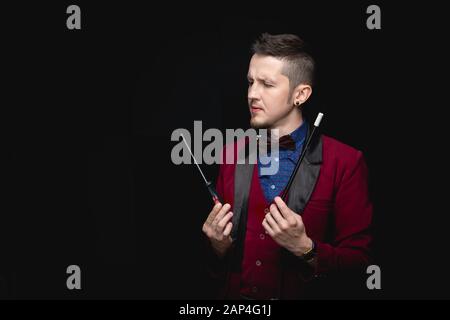 Der männliche Zauberer experimentiert mit Zauberstäben mit dem Schraubendreher-Werkzeug, schwarzer Hintergrund Stockfoto